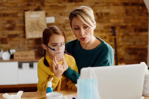 Madre inhalando a su pequeña hija con nebulizador mientras realiza una videollamada con un médico desde casa